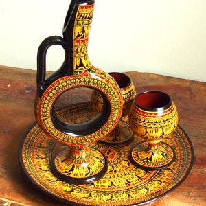May include: A black and gold painted ceramic serving set with a decorative pitcher and two cups. The set is on a matching tray with a geometric design.
