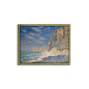 May include: A painting of a rocky cliff face along a sandy beach with blue water and a cloudy sky. The painting is framed in gold.