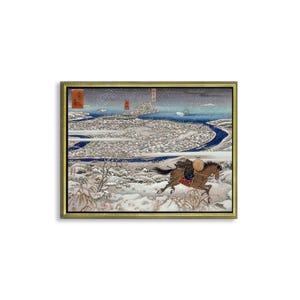 Op de afbeelding: Een Japanse houtsnede die een besneeuwd landschap met een ruiter te paard afbeeldt. De ruiter draagt een bruine hoed en een rood-witte mantel. De print is ingelijst in een gouden lijst.