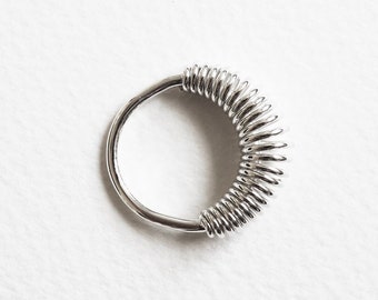 Puede incluir: Un anillo de plata con un diseño en espiral. El anillo está hecho de varios círculos pequeños conectados.