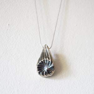 Puede incluir: Un collar de plata con un colgante en forma de l&aacute;grima. El colgante tiene un dise&ntilde;o texturizado detallado que se asemeja a una flor.