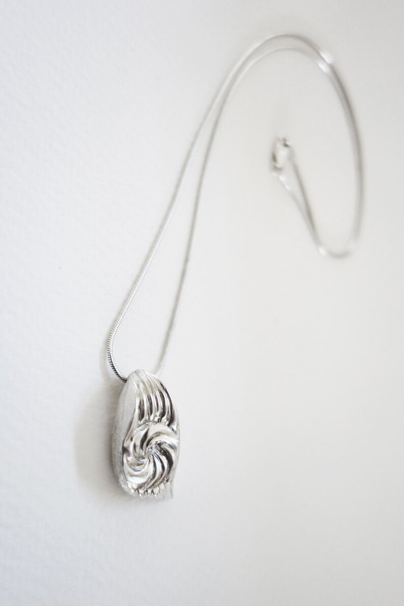 May include: A silver chain necklace with a silver pendant featuring a swirl design.