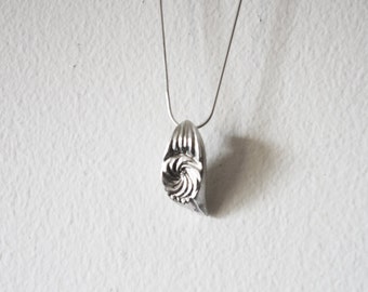 Puede incluir: Un collar de plata con un colgante en forma de espiral.