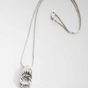 May include: A silver chain necklace with a silver pendant featuring a swirl design.