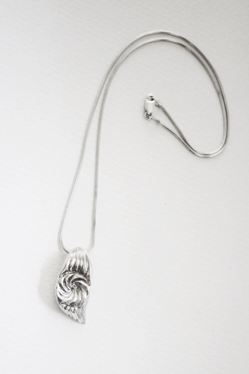 May include: A silver chain necklace with a silver pendant featuring a swirl design.