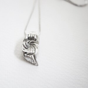 May include: A silver necklace with a swirl-shaped pendant. The pendant is made of metal and has a textured surface.