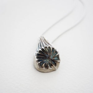Puede incluir: Un collar de plata con un colgante de flor con dise&ntilde;o detallado. La flor tiene un centro azul y p&eacute;talos plateados.