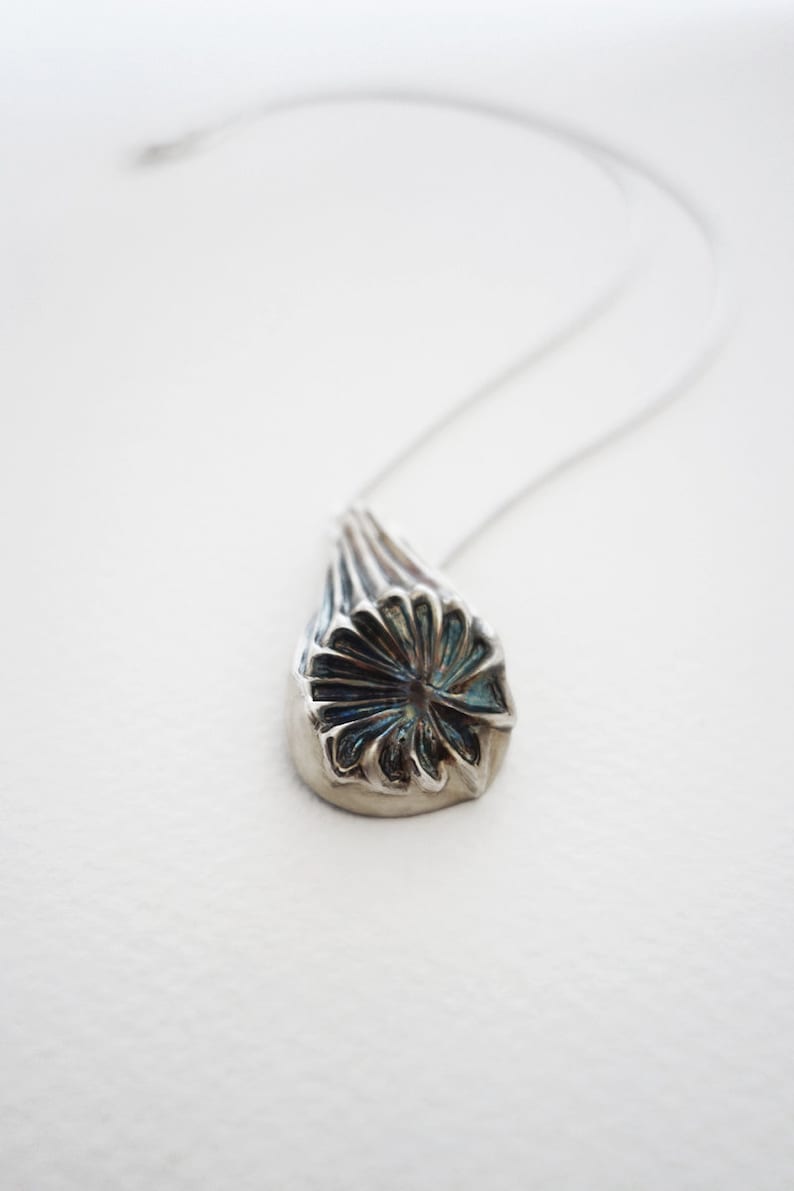 Puede incluir: Un collar de plata con un colgante de flor con dise&ntilde;o detallado. La flor tiene un centro azul y p&eacute;talos plateados.