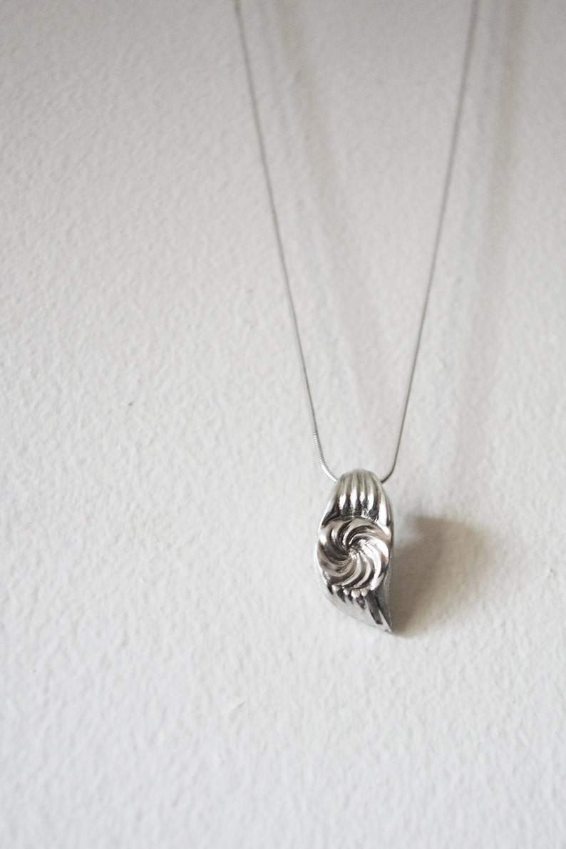 May include: A silver necklace with a swirl-shaped pendant. The pendant is made of metal and has a textured surface.
