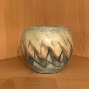 May include: A small, round ceramic vase with a blue, brown, and white glaze. The glaze has a mottled, abstract pattern.