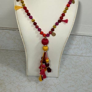 May include: A long necklace with red, orange, yellow, and purple beads, gold coin accents, and a tassel with multiple layers of red, orange, and yellow fabric.