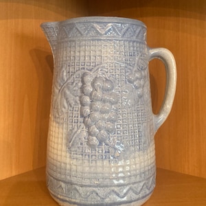 May include: A blue and white glazed ceramic pitcher with a woven pattern and a grape design. The pitcher has a handle and a spout.
