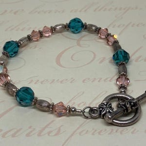 May include: A silver bracelet with teal and pink beads and a silver toggle clasp.
