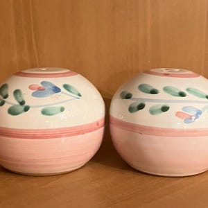 May include: A pair of ceramic salt and pepper shakers shaped like eggs. The shakers are painted white with pink, green and blue floral designs.