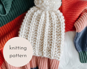 May include: White knitted beanie with a pom pom on top. The beanie is laying on a multi-colored striped sweater. The text "knitting pattern" is written on a circle in the foreground.