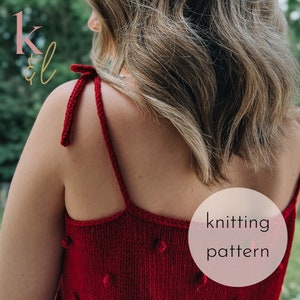 May include: A red knitted top with tie straps and a textured design. The top features a round neckline and small, raised bobbles. The words "knitting pattern" are in a white circle. The top is a handmade item.