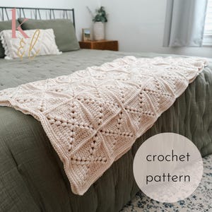 Peut inclure: Une couverture au crochet de couleur crème avec un motif géométrique est drapée sur un lit. La couverture présente un motif répétitif de carrés et de motifs floraux. Les mots "crochet pattern" sont dans un cercle en bas à droite.