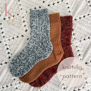 Puede incluir: Tres calcetines tejidos en tonos verdes, naranjas y rojos, colocados sobre una superficie blanca texturizada. Los calcetines están hechos a mano, con patrones de puntadas visibles. Incluye el texto "knitting pattern".