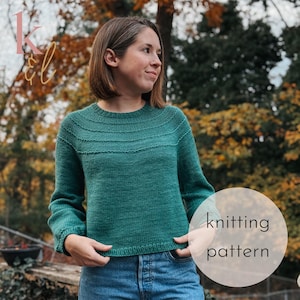 May include: A teal green knitted sweater with a round neckline and ribbed detailing. The sweater is paired with blue jeans. A circular graphic with the words "knitting pattern" is in the lower right corner.