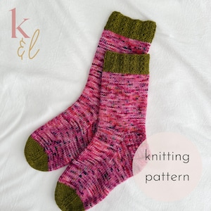 Pode incluir: Um par de meias de tricô rosa e verde com um padrão de trança na bainha. As meias são feitas com um fio salpicado e têm um calcanhar e uma ponta verdes.