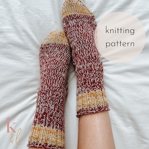 Pode incluir: Um par de meias de tricô em um esquema de cores vermelho, branco e amarelo. As meias têm uma textura canelada e uma faixa contrastante na parte superior. O texto "knitting pattern" é visível na imagem.