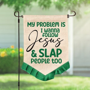 K&ouml;nnte beinhalten: Eine beige Gartenflagge in Jute-Optik mit gr&uuml;nem und schwarzem Text, der lautet: MY PROBLEM IS I WANNA FOLLOW JESUS & SLAP PEOPLE too. Die Flagge hat einen spitz zulaufenden unteren Rand mit einer plissierten gr&uuml;nen Stoffborte.