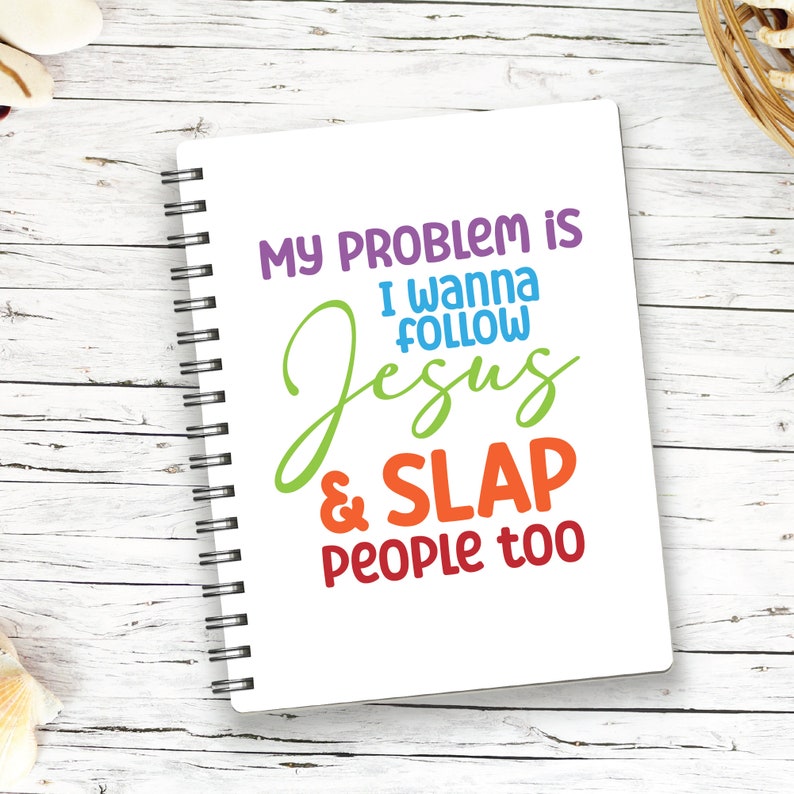 K&ouml;nnte beinhalten: Ein wei&szlig;es Notizbuch mit Spiralbindung und dem farbigen Aufdruck: MY PROBLEM IS I WANNA FOLLOW Jesus & SLAP PEOPLE too. Die W&ouml;rter sind in Lila, Blau, Gr&uuml;n, Orange und Rot gedruckt, mit einer schwarzen Metallspirale an der linken Seite.