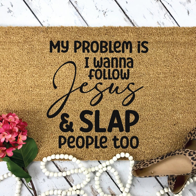 K&ouml;nnte beinhalten: Eine rechteckige, beigefarbene Kokosfasermatte mit schwarzem Text: MY PROBLEM IS I WANNA FOLLOW JESUS & SLAP PEOPLE too. Die Matte ist mit einem Strau&szlig; rosa Hortensien, einer wei&szlig;en Holzperlenkette und Schuhen mit Leopardenmuster verziert.