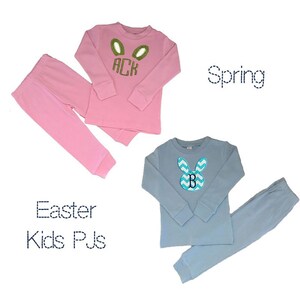 May include: Two sets of children's pajamas. One set is pink with green bunny ears and the letters "ACK". The other set is light blue with a chevron bunny design and the letter "B". The text "Easter Kids PJs" and "Spring" are also visible.