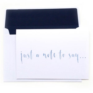 Könnte beinhalten: Eine weiße Karte mit einem dunkelblauen Umschlag. Die Karte trägt den Text "just a note to say..." in blauer Tinte.