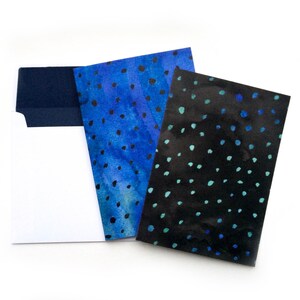 May include: Two cards with blue and black watercolor patterns of dots. The cards are on top of a white envelope with a navy blue flap.