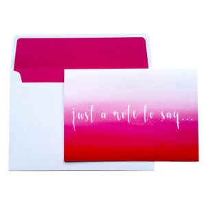 May include: A white card with a pink ombre design and the text "just a note to say..." in white script.