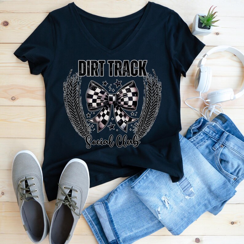 Pu&ograve; includere: T-shirt nero con scollo a V con grafica "Dirt Track Social Club". La grafica presenta un fiocco a scacchi, stelle e un design a ghirlanda. Anche le scarpe da ginnastica grigie e i jeans blu sono nell'immagine.