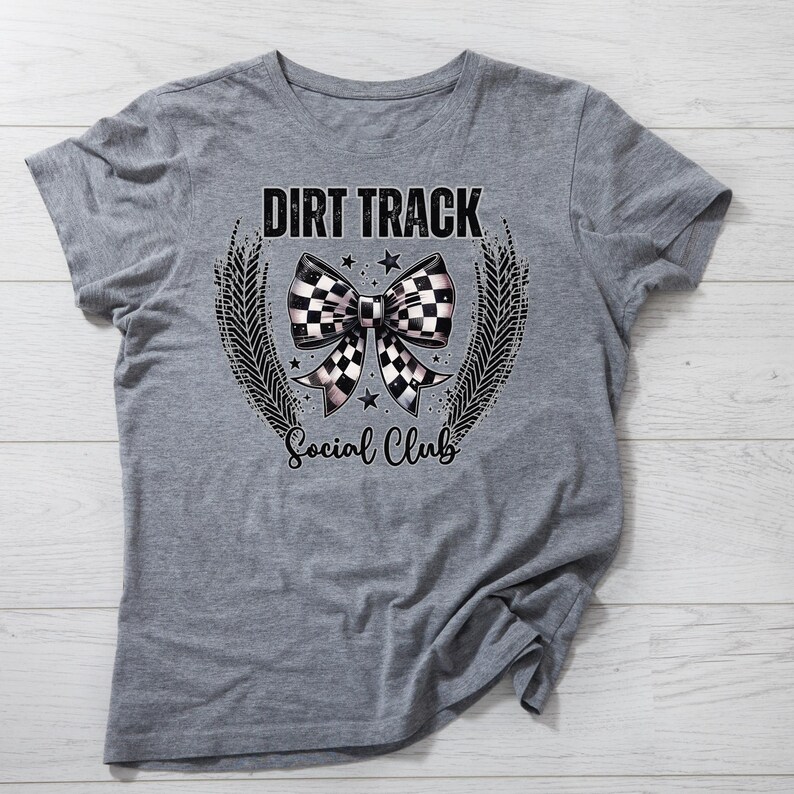 Pu&ograve; includere: Una maglietta grigia con la scritta "DIRT TRACK" sopra un disegno a fiocco a scacchi. Sotto il fiocco, il testo recita "Social Club". Il disegno &egrave; incorniciato da una ghirlanda di foglie e stelle.