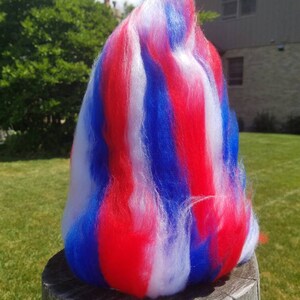 May include: A pile of red, white, and blue fiber, resembling a fluffy cloud, sits on a wooden stump.