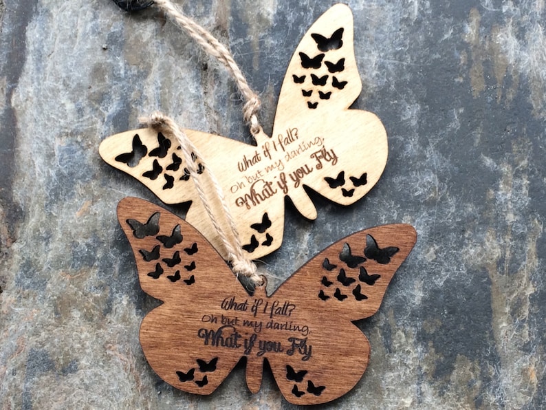 May include: Two wooden butterfly ornaments with a cutout design. The butterflies are painted in shades of brown and have the text "What if I fall? Oh but my darling, What if you fly" engraved on them.