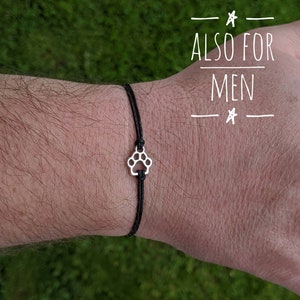 Here is a cute paw print wish bracelet. The paw print is silver and has black waxed cotton cord attached on the top and bottom. It is tied on to a man's wrist because the bracelet is also for men.