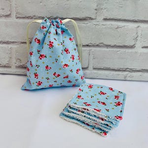 May include: A set of six reusable cotton makeup remover pads in a light blue floral print with white trim. The pads are stacked and come in a matching drawstring bag.