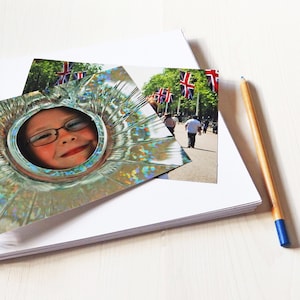 May include: A child's face is visible through a hole in a silver, iridescent, circular object. The child is smiling and has brown hair and brown eyes. The background is a blurry image of a street scene with British flags.