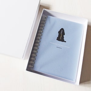 May include: A light blue journal with a black silhouette of a dog and the text "Christine Jane Williamson Journal" on the cover.