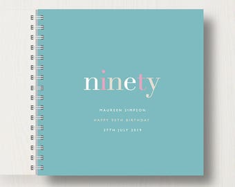 Könnte beinhalten: Ein türkisfarbenes Spiralbuch mit dem Wort "ninety" in rosa und weiß. Der Text "Maureen Simpson Happy 90th Birthday 27th July 2019" ist unter dem Wort "ninety" gedruckt.