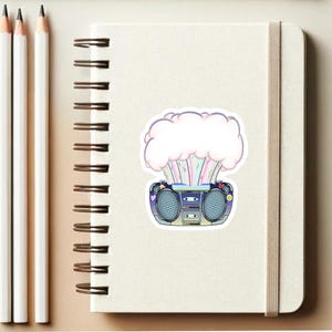 May include: A sticker featuring a retro boombox with a pink and white cloud exploding out of the top. The boombox has a blue and black design with colorful buttons and a cassette tape slot.