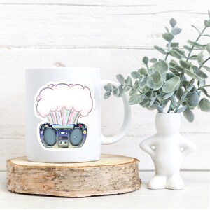 May include: White ceramic mug with a colorful graphic of a boombox with a pink cloud exploding from it. The graphic has a retro style.