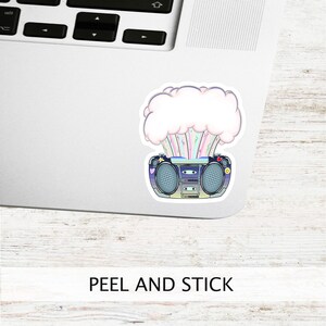 May include: A sticker featuring a retro boombox with a rainbow explosion coming out of it. The boombox is blue and black with a white background. The sticker says "PEEL AND STICK" at the bottom.