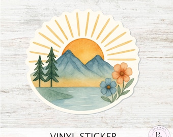 May include: A round vinyl sticker featuring a watercolor landscape. The design includes a rising sun, mountains, trees, a lake, and flowers in shades of orange, blue, and green. The text "VINYL STICKER" is printed at the bottom.