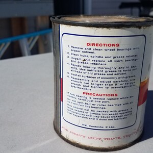 May include: A white metal can with red and blue text and a red stripe. The can contains heavy duty truck grease. The can has directions and precautions for using the grease.