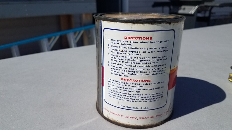 May include: A white metal can with red and blue text and a red stripe. The can contains heavy duty truck grease. The can has directions and precautions for using the grease.