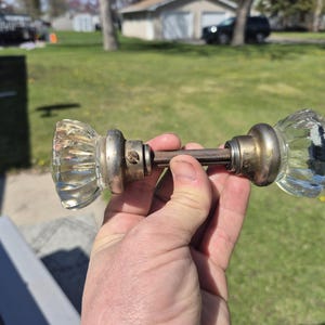 May include: A vintage glass door knob with a ribbed design. The knob has a clear, faceted glass appearance with a metal base and connecting rod. The metal components show signs of age and wear.