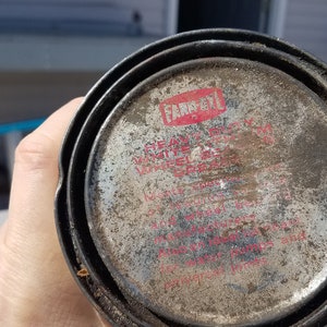 May include: Close-up of a silver can with a red and white label that reads "Farboil" "Heavy Duty" "White" "Waterproof" "Grease" "For use on all metal surfaces, including boat hulls and motor pumps and implements".
