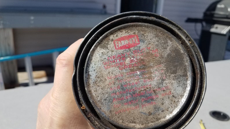 May include: Close-up of a silver can with a red and white label that reads "Farboil" "Heavy Duty" "White" "Waterproof" "Grease" "For use on all metal surfaces, including boat hulls and motor pumps and implements".